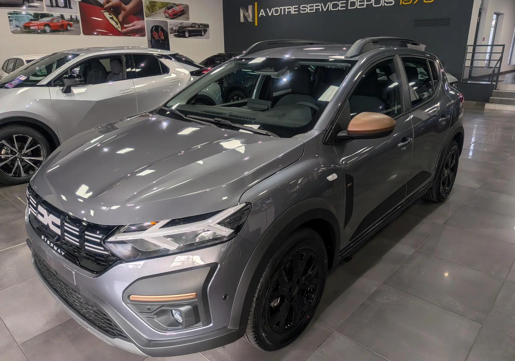 Vue 3/4 avant droite d'une Dacia Sandero Stepway TCe 110 Gris Schiste avec rétroviseurs couleur cuivre en showroom.