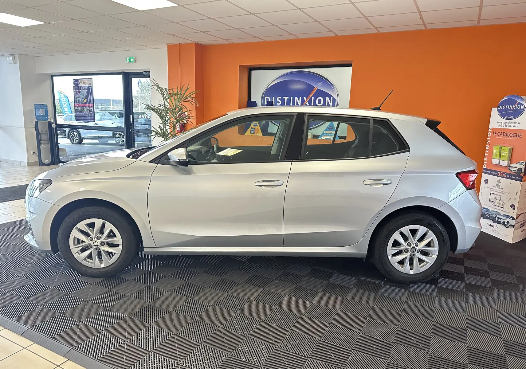 Vue de profil côté gauche d'une Skoda Fabia Ambition gris argent 2023 en intérieur showroom.
