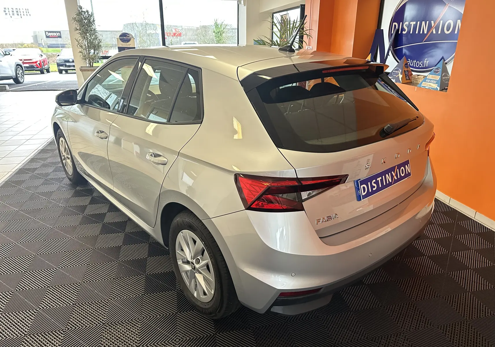 Vue 3/4 arrière droite d'une Skoda Fabia Ambition gris argent 2023 en essence, stationnée en intérieur sur sol noir texturé.