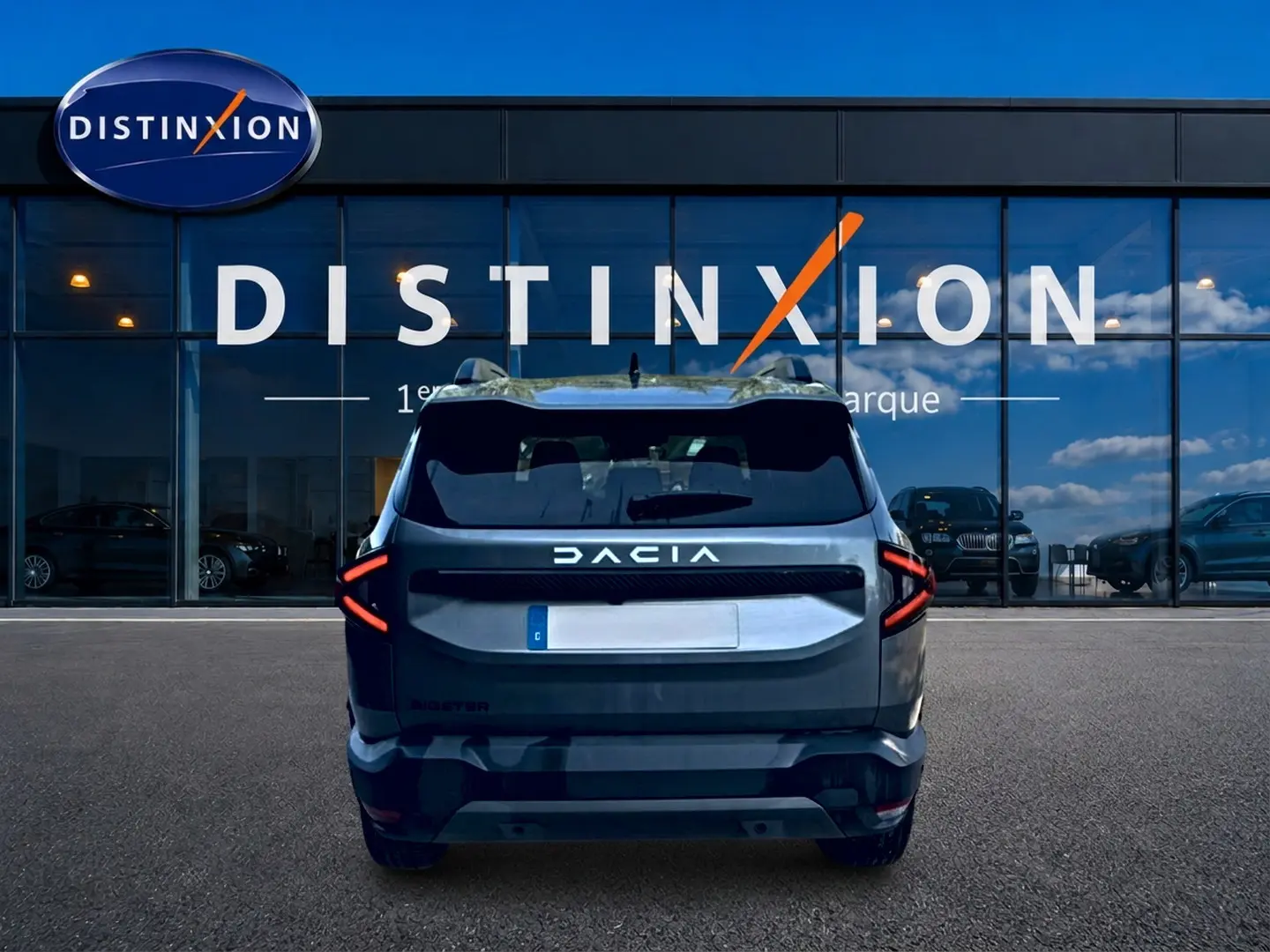Vue arrière d'un Dacia Bigster gris schiste garé devant une vitrine avec logo Distinxion, feux arrière LED en forme de flèche.