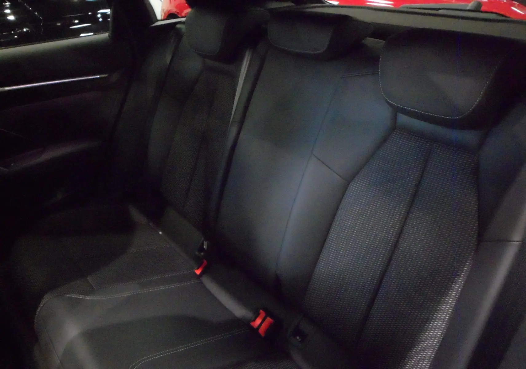 Vue intérieure des sièges arrière en cuir noir de l'Audi A3 Sportback 35 TFSI S-Line 2025, avec ceintures rouges visibles.