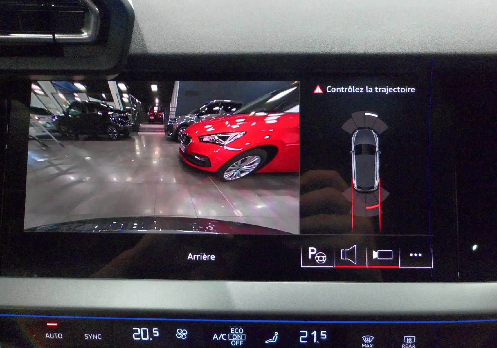 Vue de l'écran de recul de l'Audi A3 Sportback gris Daytona montrant une voiture rouge en parking intérieur.