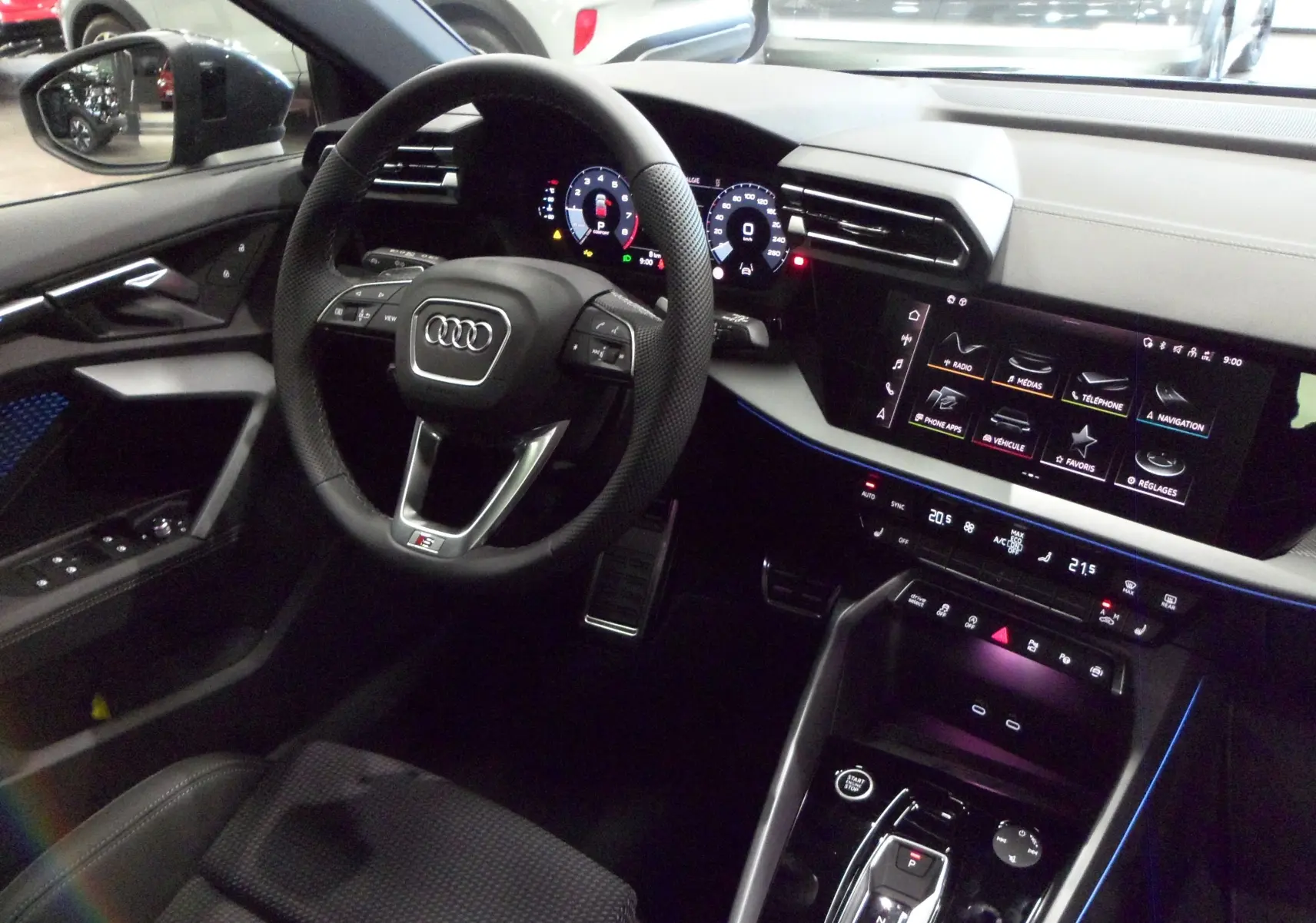 Vue intérieure côté conducteur de l'Audi A3 Sportback 35 TFSI 150 S-Line 2025 avec tableau de bord numérique et ambiance lumineuse bleue