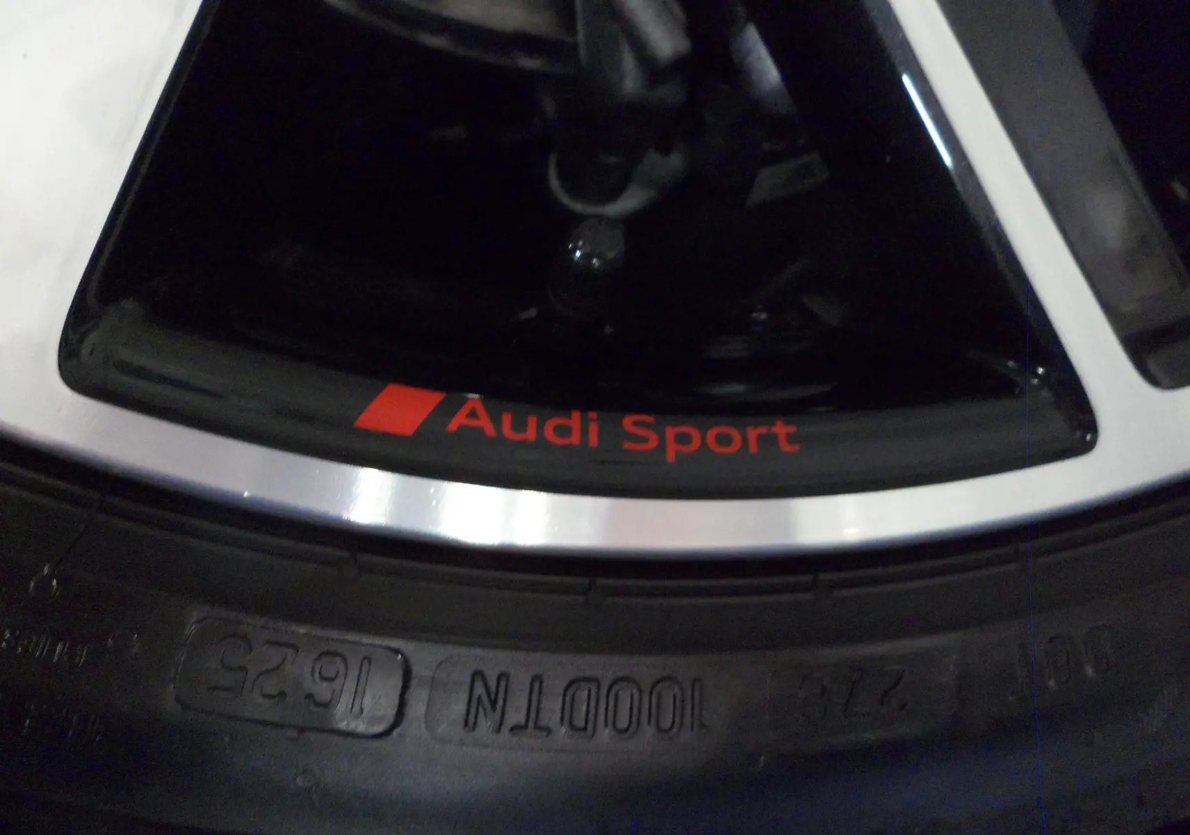 Gros plan sur la jante Audi Sport avec lettrage rouge, soulignant le caractère sportif du modèle A3 Sportback gris Daytona.