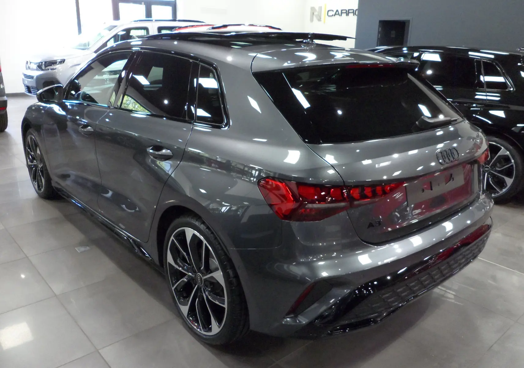 Audi A3 Sportback gris Daytona vue 3/4 arrière droit en showroom avec jantes noires bicolores distinctives