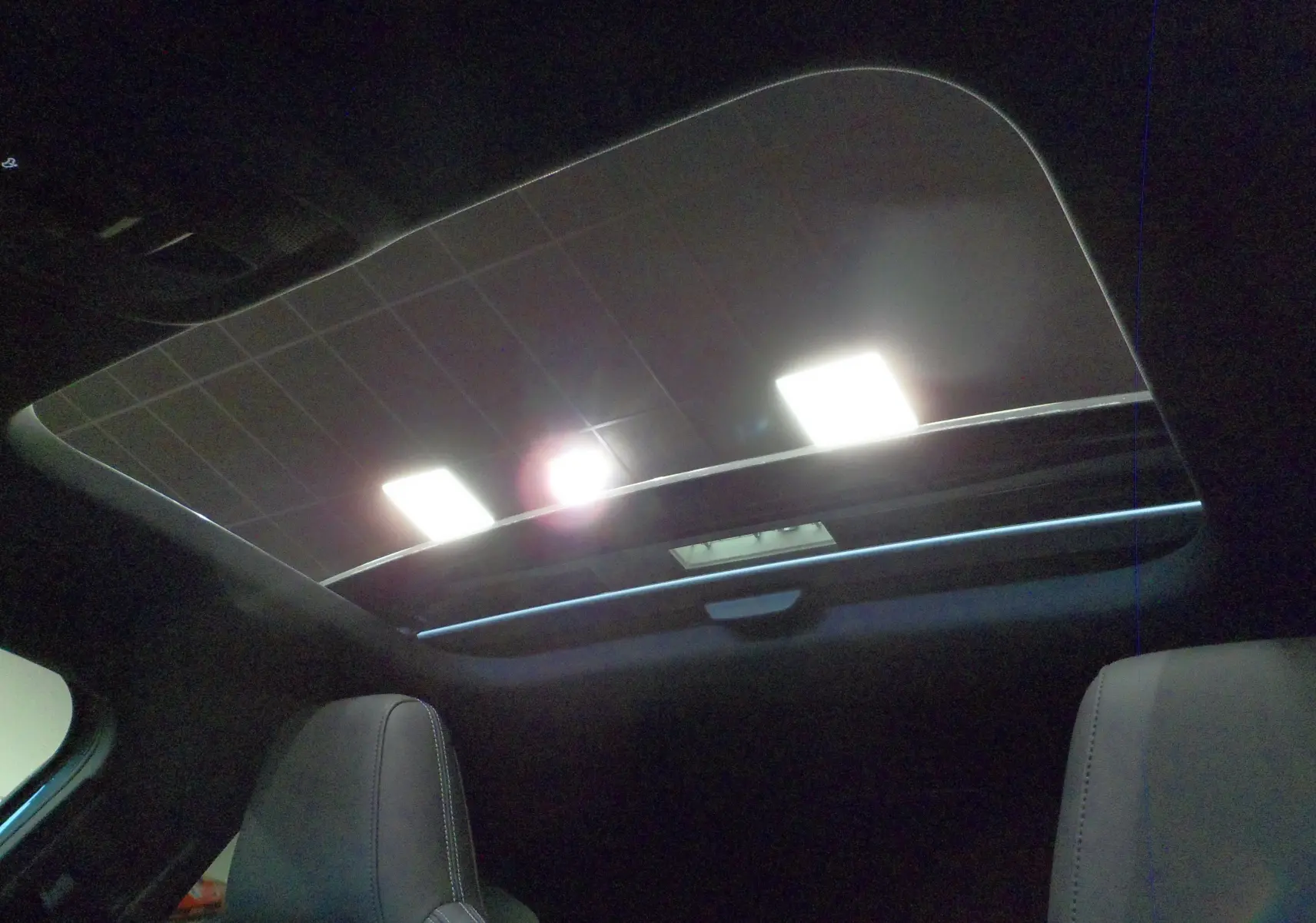 Toit panoramique ouvert vu de l'intérieur arrière de l'Audi A3 Sportback 35 TFSI gris Daytona avec sièges en cuir noir.