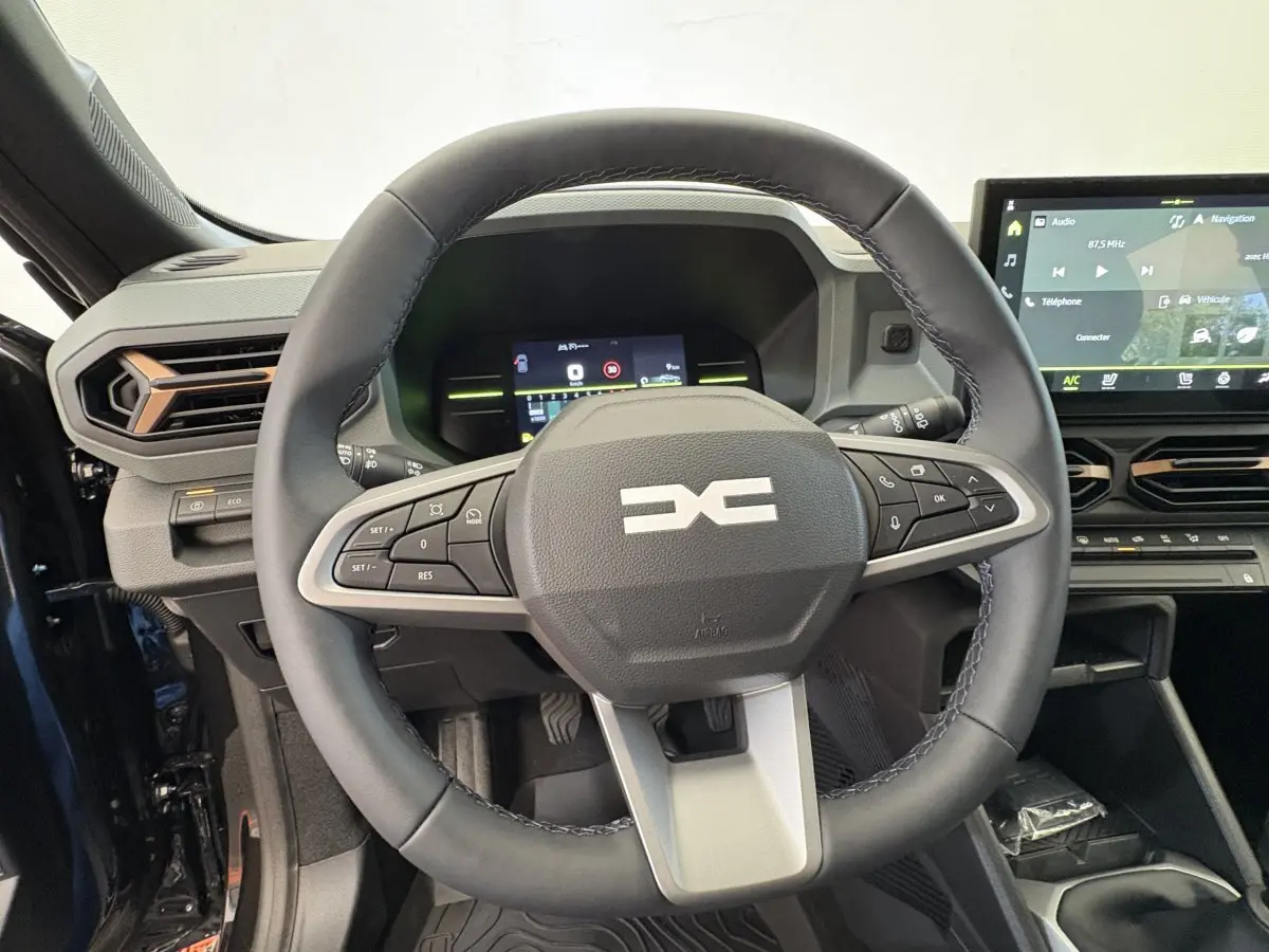 Vue intérieure centrée sur le volant cuir noir du Dacia Duster 2025 avec tableau de bord digital et écran tactile.
