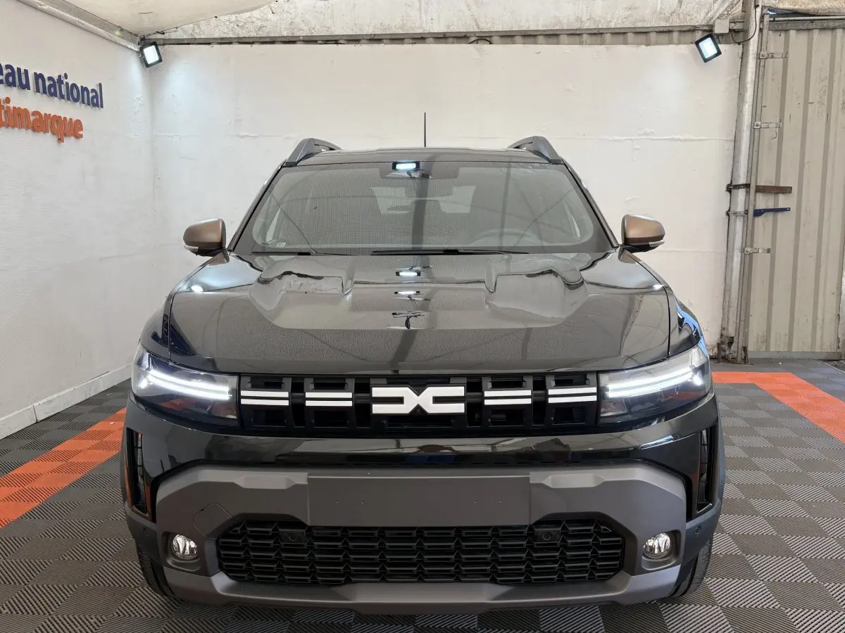Vue frontale d'un Dacia Duster noir 2025 avec phares LED allumés et calandre distinctive au logo central.
