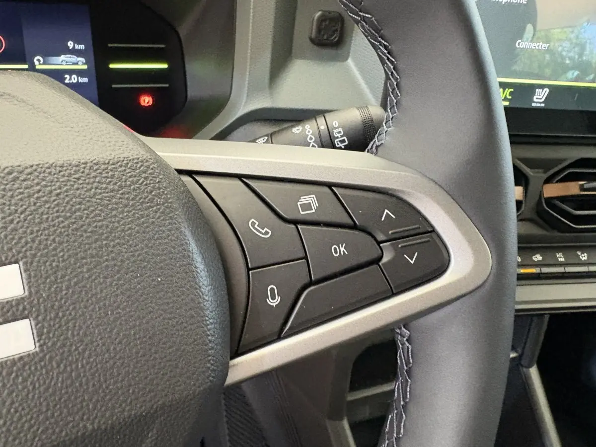 Gros plan sur le côté droit du volant noir du Dacia Duster 2025 avec commandes multifonctions et écran tactile en arrière-plan