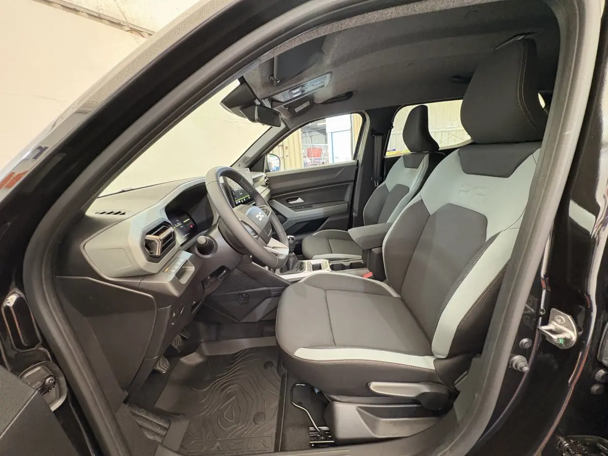 Intérieur avant droit du Dacia Duster noir 2025, sièges bicolores gris et noir avec volant multifonctions en vue latérale.