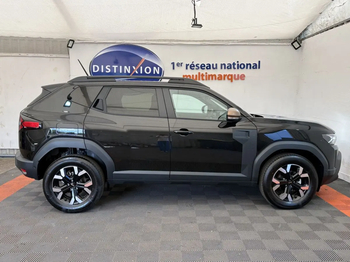 Profil côté gauche du Dacia Duster noir 2025 avec jantes alliage bicolores et barres de toit noires.