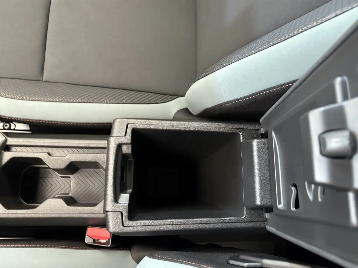 Gros plan sur la console centrale ouverte du Dacia Duster noir 2025, montrant le rangement intérieur et les sièges tissu gris.