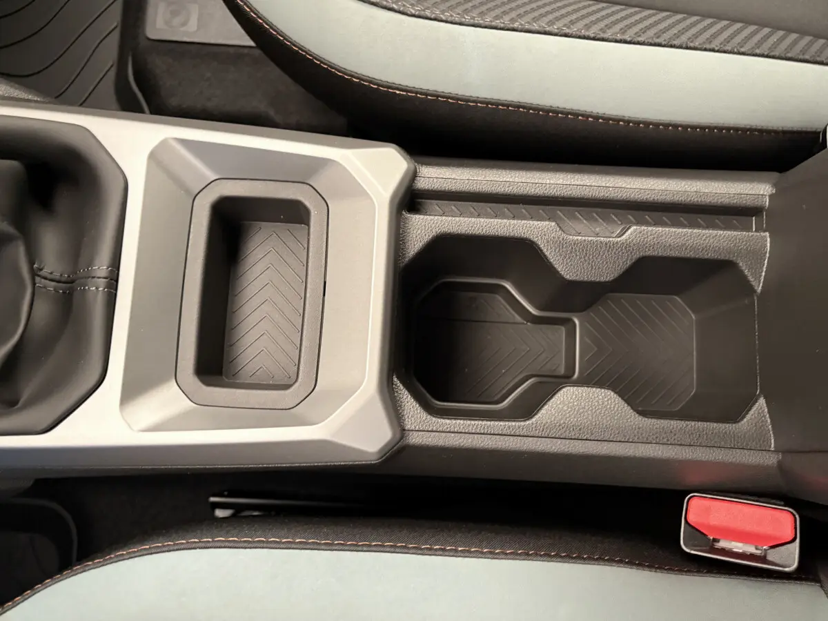 Gros plan sur la console centrale du Dacia Duster 2025 noir, avec porte-gobelets et surpiqûres orange sur les sièges.