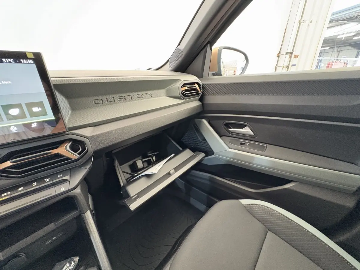 Intérieur côté passager du Dacia Duster noir 2025, tableau de bord avec boîte à gants ouverte et écran tactile visible.