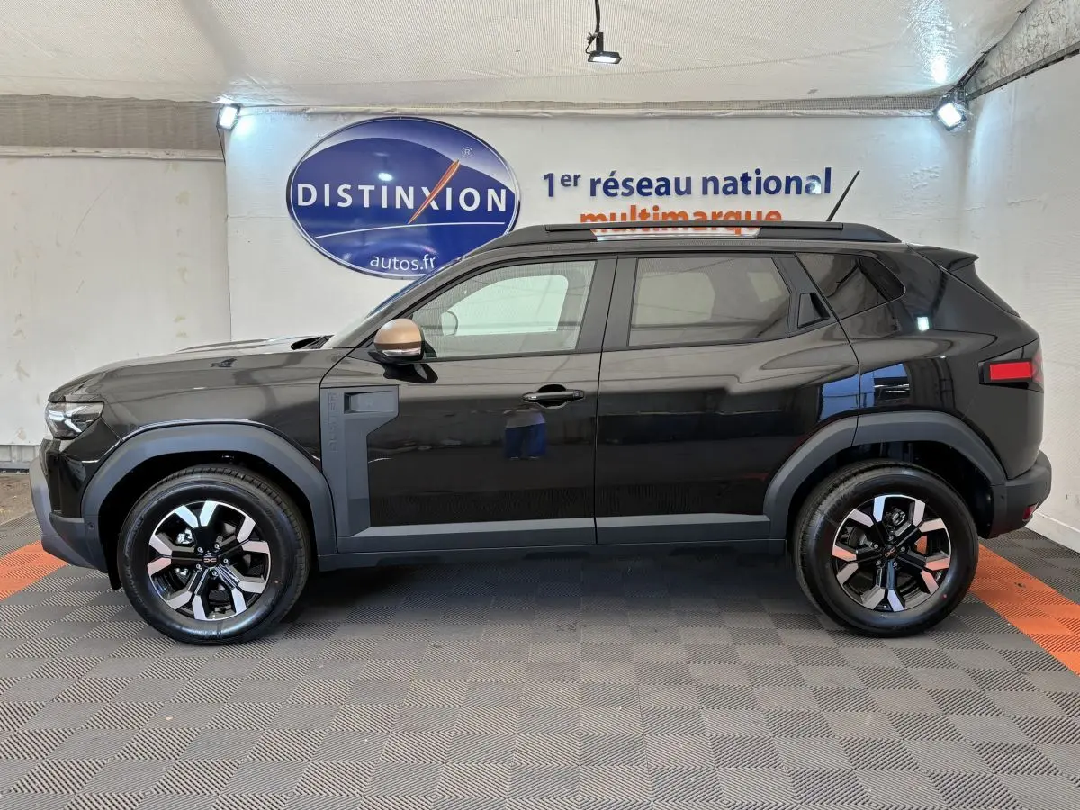 Profil côté gauche du Dacia Duster noir 2025 avec jantes bicolores et barres de toit noires en intérieur showroom.