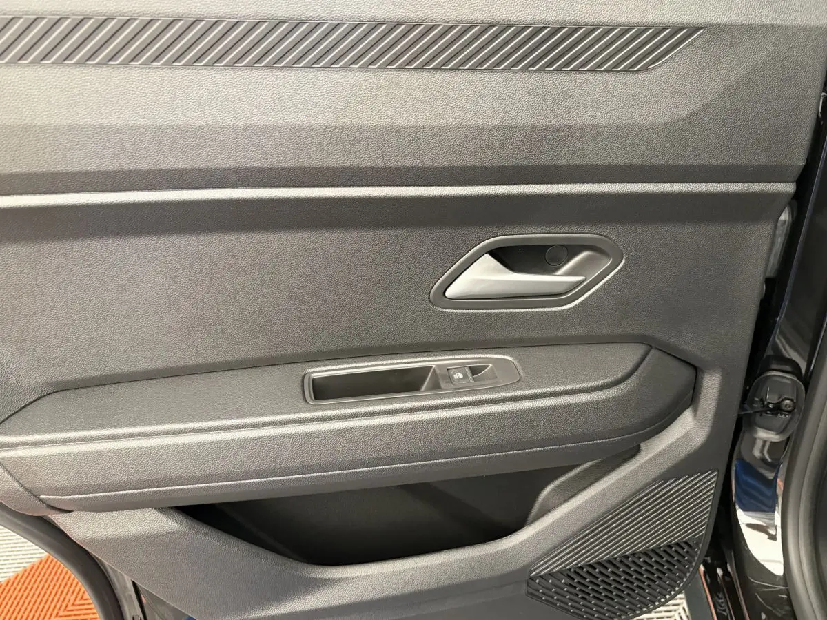 Vue rapprochée de la porte intérieure côté conducteur du Dacia Duster noir, avec poignée et commande de fenêtre.