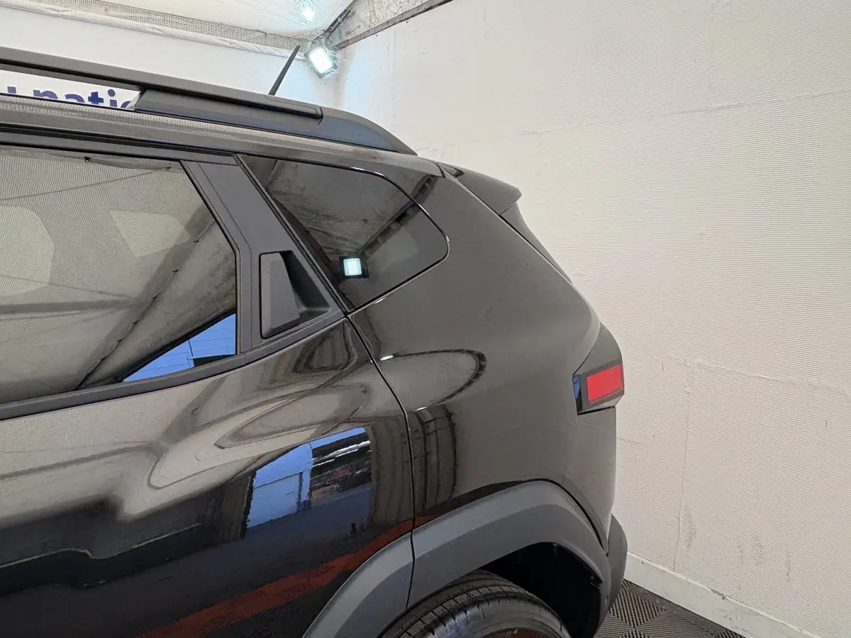 Vue arrière côté gauche du Dacia Duster noir 2025 avec feux arrière rectangulaires et barres de toit noires.