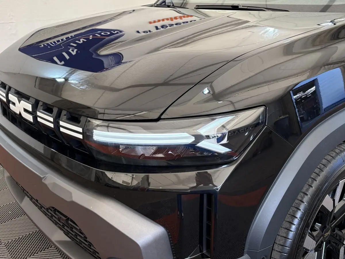 Gros plan sur l'avant droit du Dacia Duster noir 2025, mettant en valeur le phare LED et la calandre distinctive.