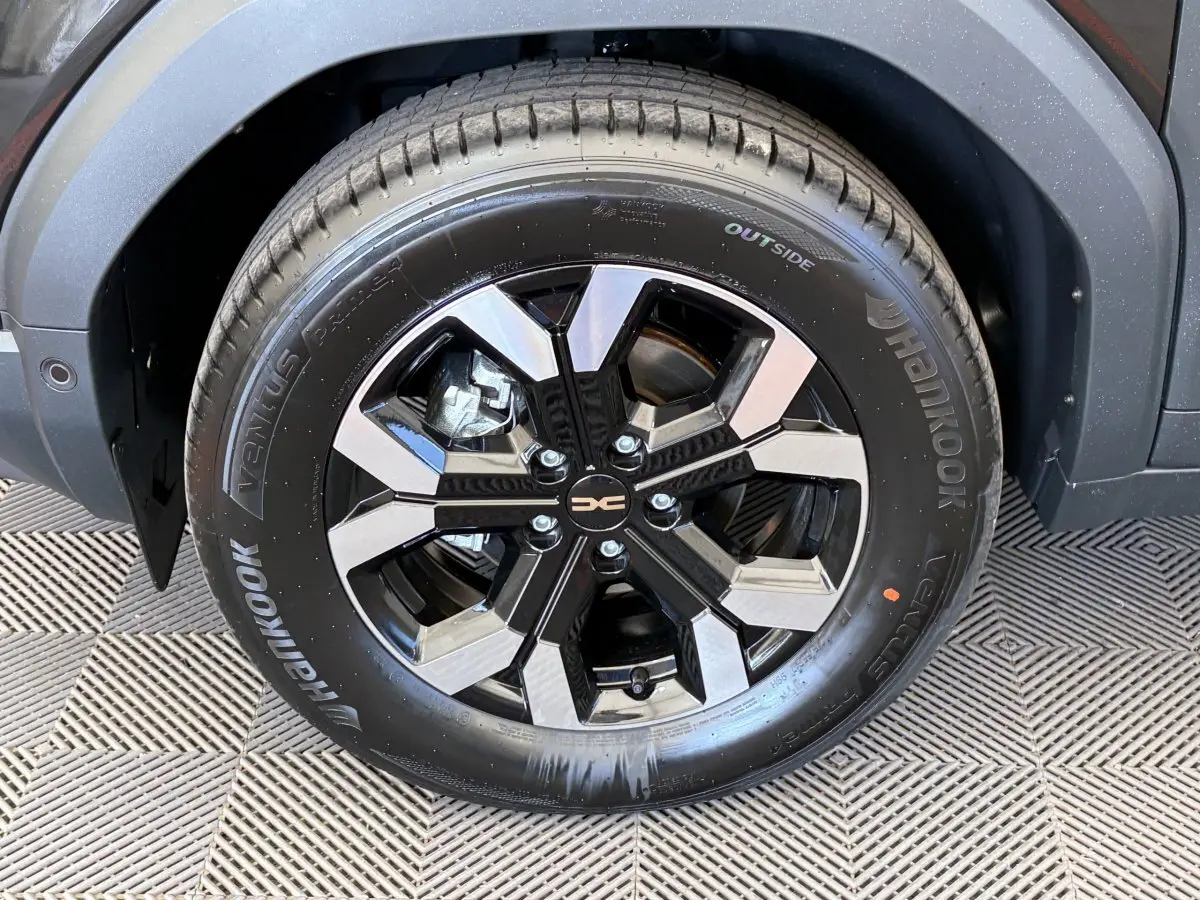 Gros plan sur la roue avant droite noire du Dacia Duster 2025 avec jante alliage bicolore et logo central.