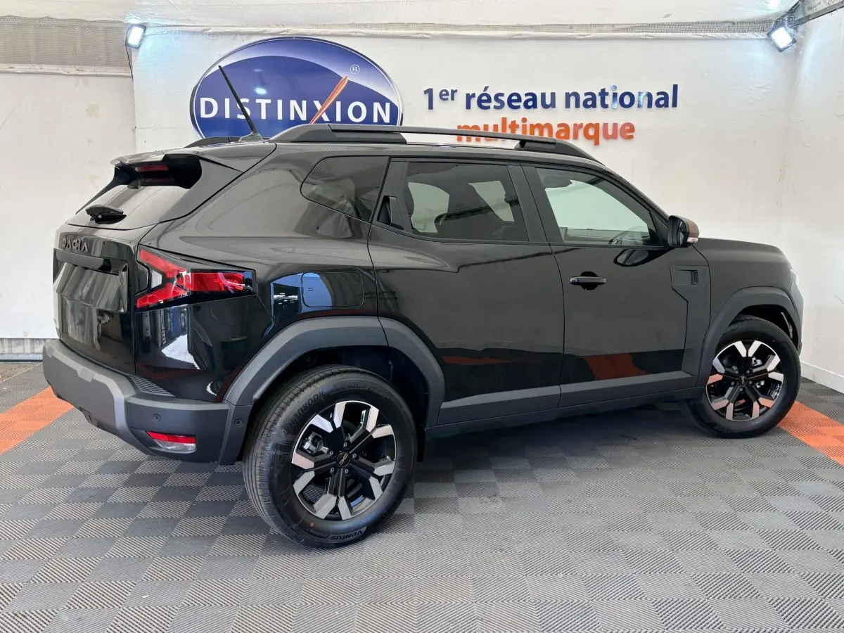 Vue latérale droite du Dacia Duster noir 2025 avec jantes alliage et barres de toit noires dans un showroom.