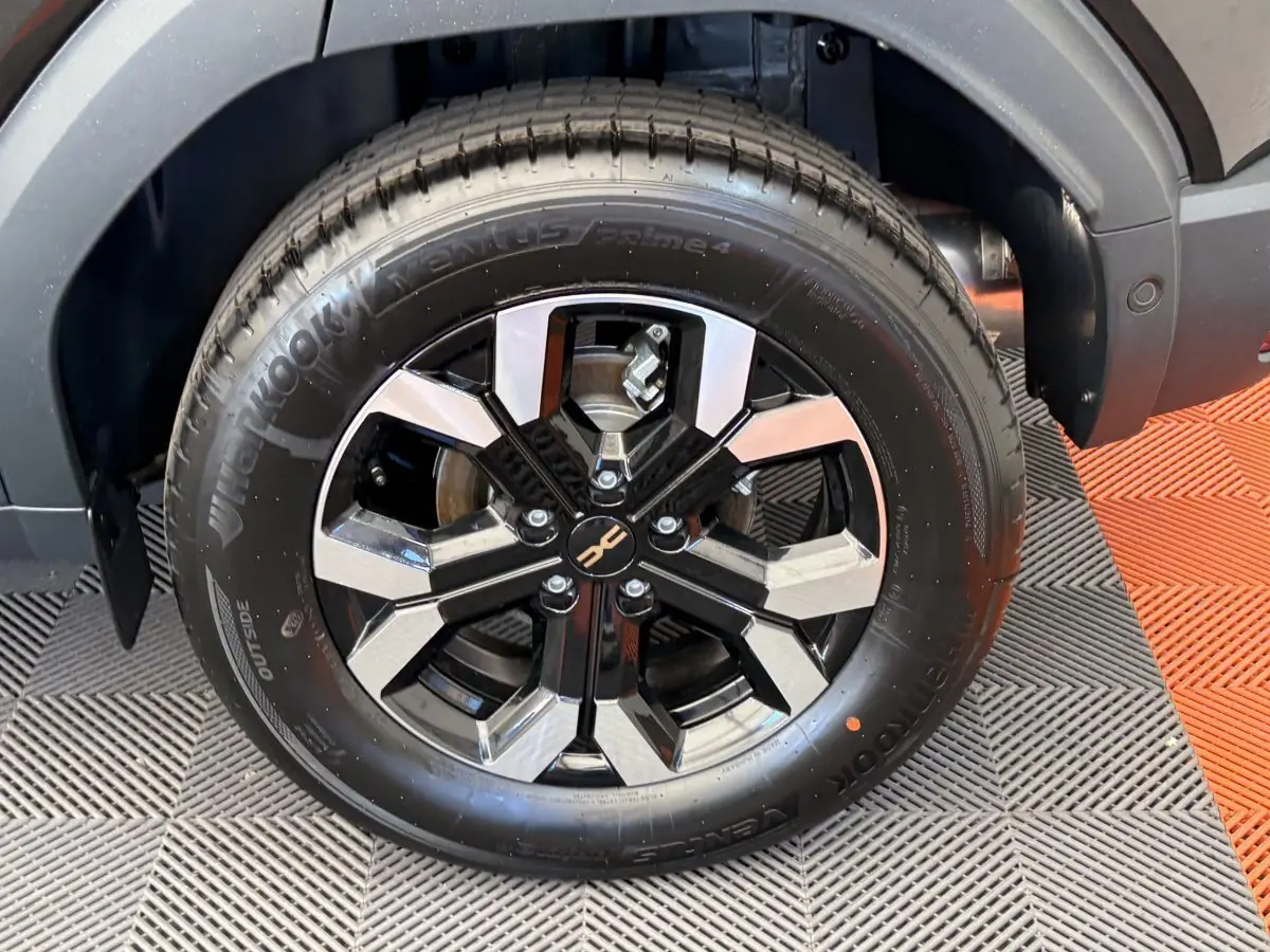 Gros plan sur la roue avant droite du Dacia Duster noir 2025 avec jante alliage bicolore et logo central distinctif.