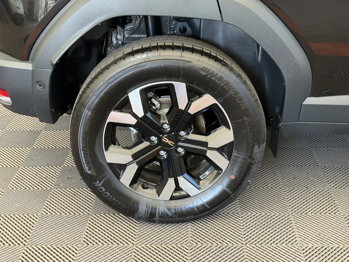 Gros plan sur la roue arrière gauche du Dacia Duster noir 2025, mettant en valeur la jante alliage bicolore moderne.