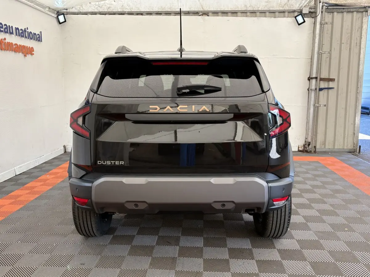 Vue arrière du Dacia Duster noir 2025 avec logo doré et feux arrière en forme de C, stationné en intérieur.