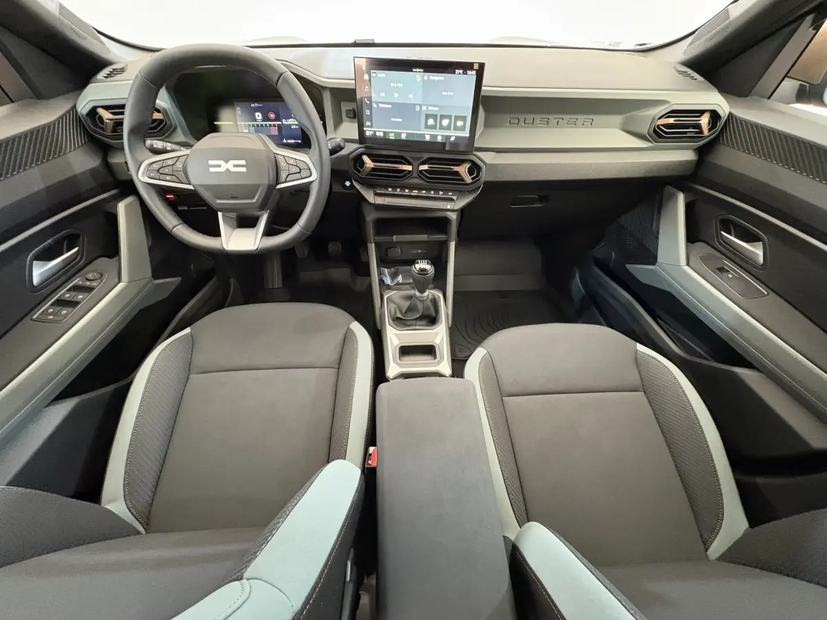 Vue intérieure avant du Dacia Duster 2025 noir, volant multifonctions, écran tactile central et boîte manuelle.