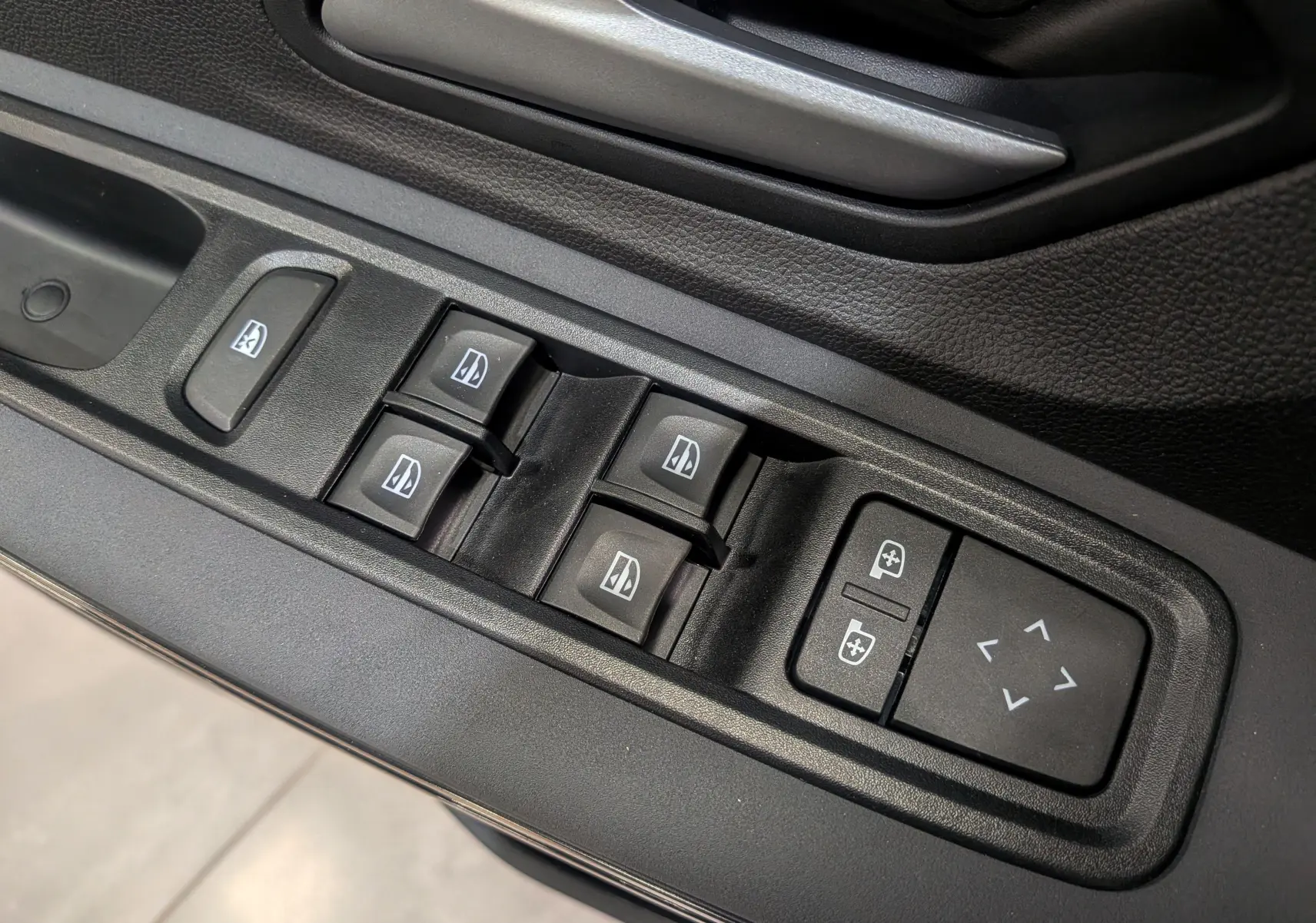 Gros plan sur les commandes de lève-vitres et réglage des rétroviseurs côté conducteur d'une Dacia Sandero Stepway 2025.