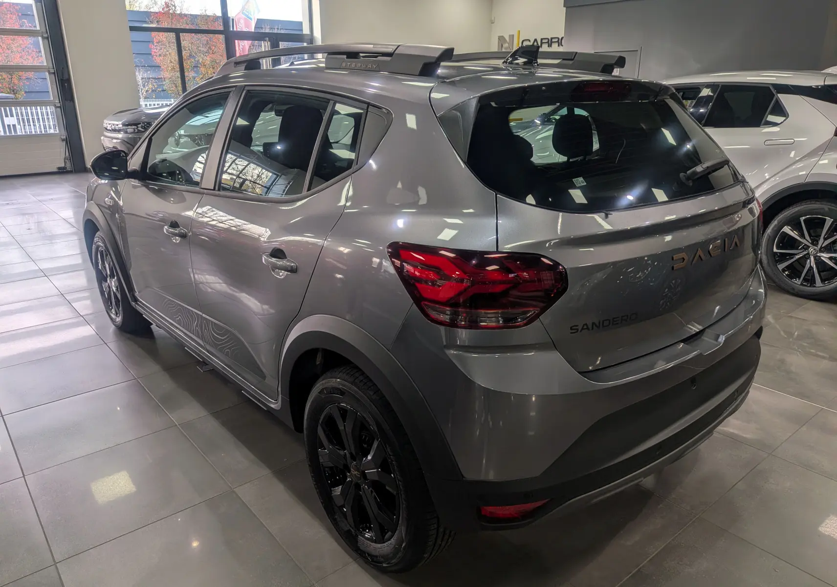 Vue 3/4 avant gauche d'une Dacia Sandero Stepway TCe 110 gris schiste en showroom avec jantes alliage noires.