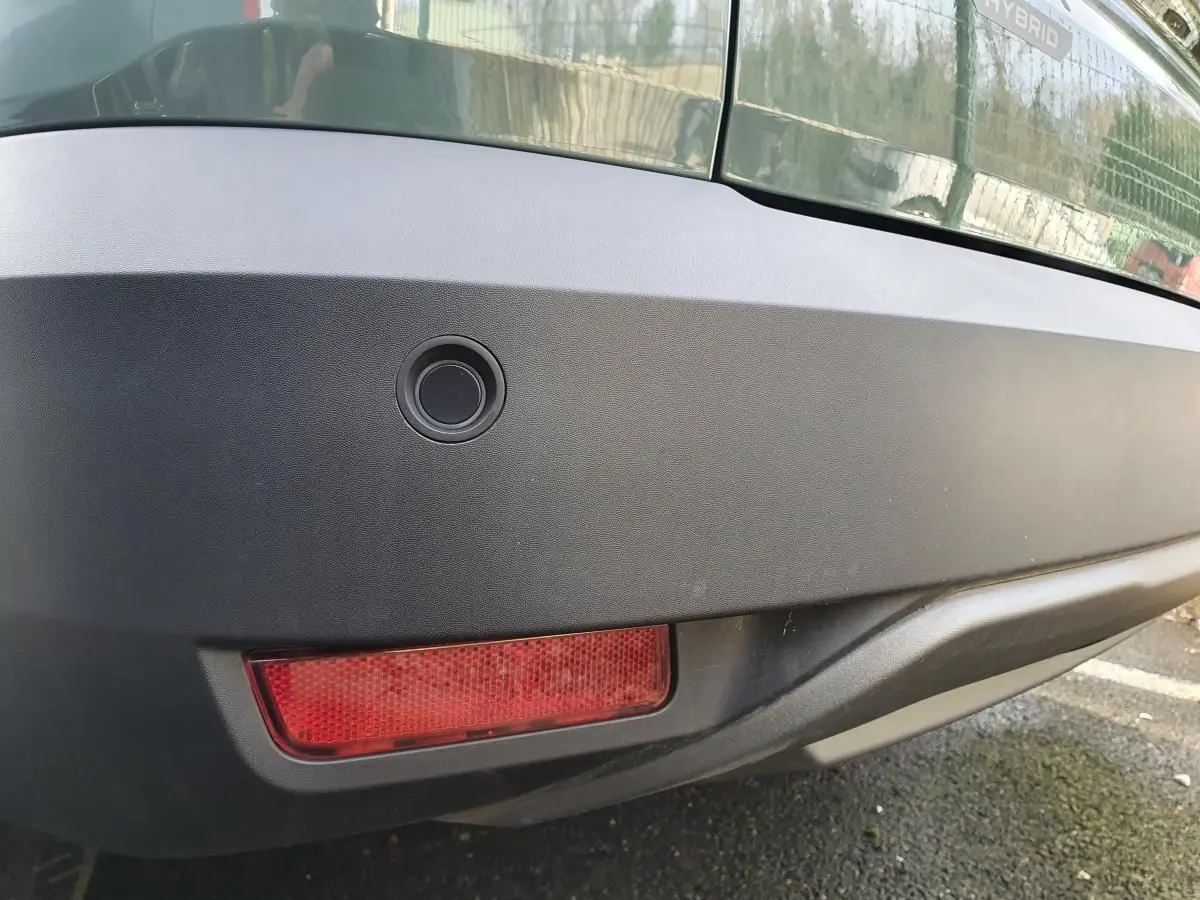 Gros plan sur le pare-chocs arrière kaki métallisé du Dacia Jogger 1.6 Hybrid avec capteur de recul et feu antibrouillard.