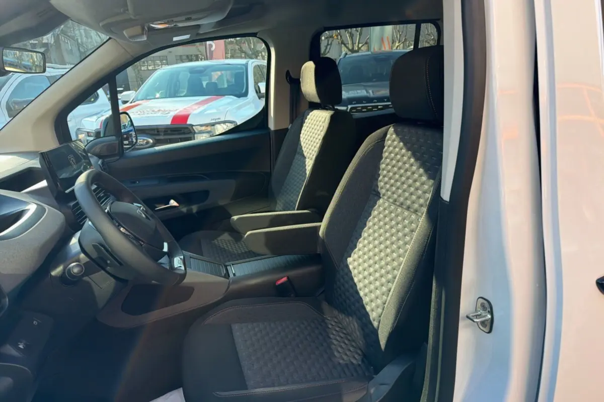 Vue intérieure côté gauche du Peugeot Rifter blanc kaolin 2025, mettant en valeur les sièges tissu avec accoudoirs centraux.