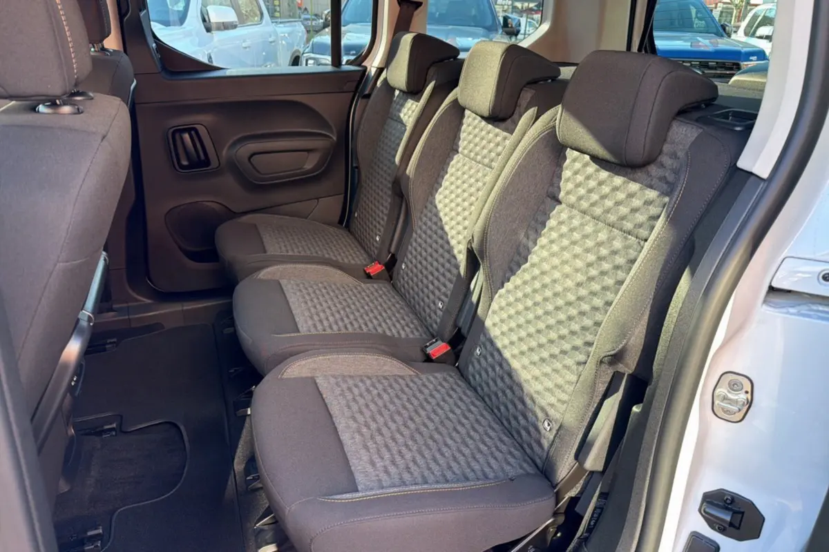 Vue latérale des sièges arrière en tissu gris du Peugeot Rifter Blanc Kaolin 2025, porte arrière ouverte.