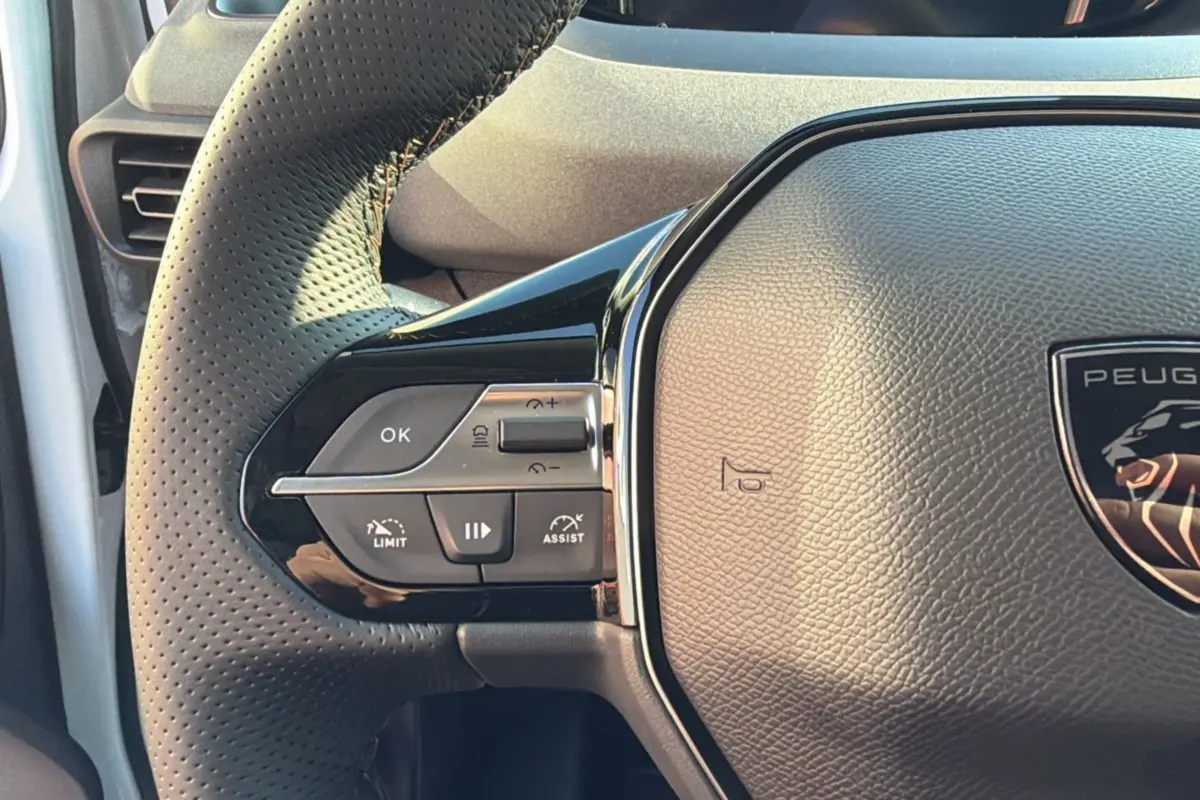 Gros plan sur le volant cuir perforé du Peugeot Rifter blanc kaolin, avec commandes multifonctions et logo lion central.