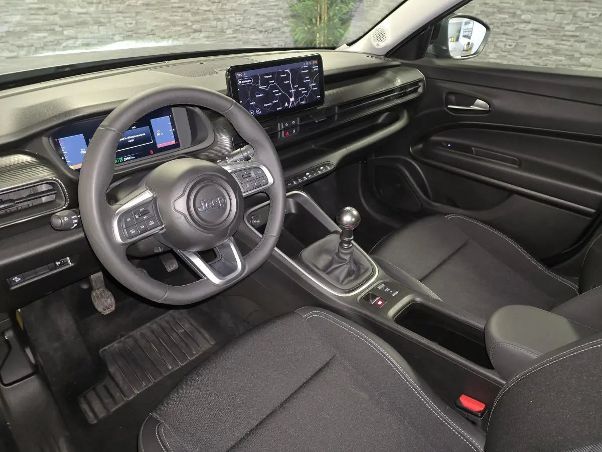 Vue intérieure côté conducteur du Jeep Avenger 2025, tableau de bord noir avec écran tactile et levier de vitesses manuel.