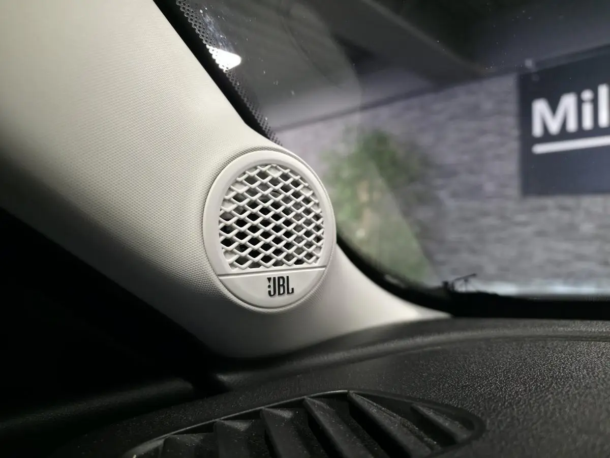 Gros plan sur l'enceinte JBL blanche intégrée à l'angle gauche du tableau de bord noir du Jeep Avenger gris.