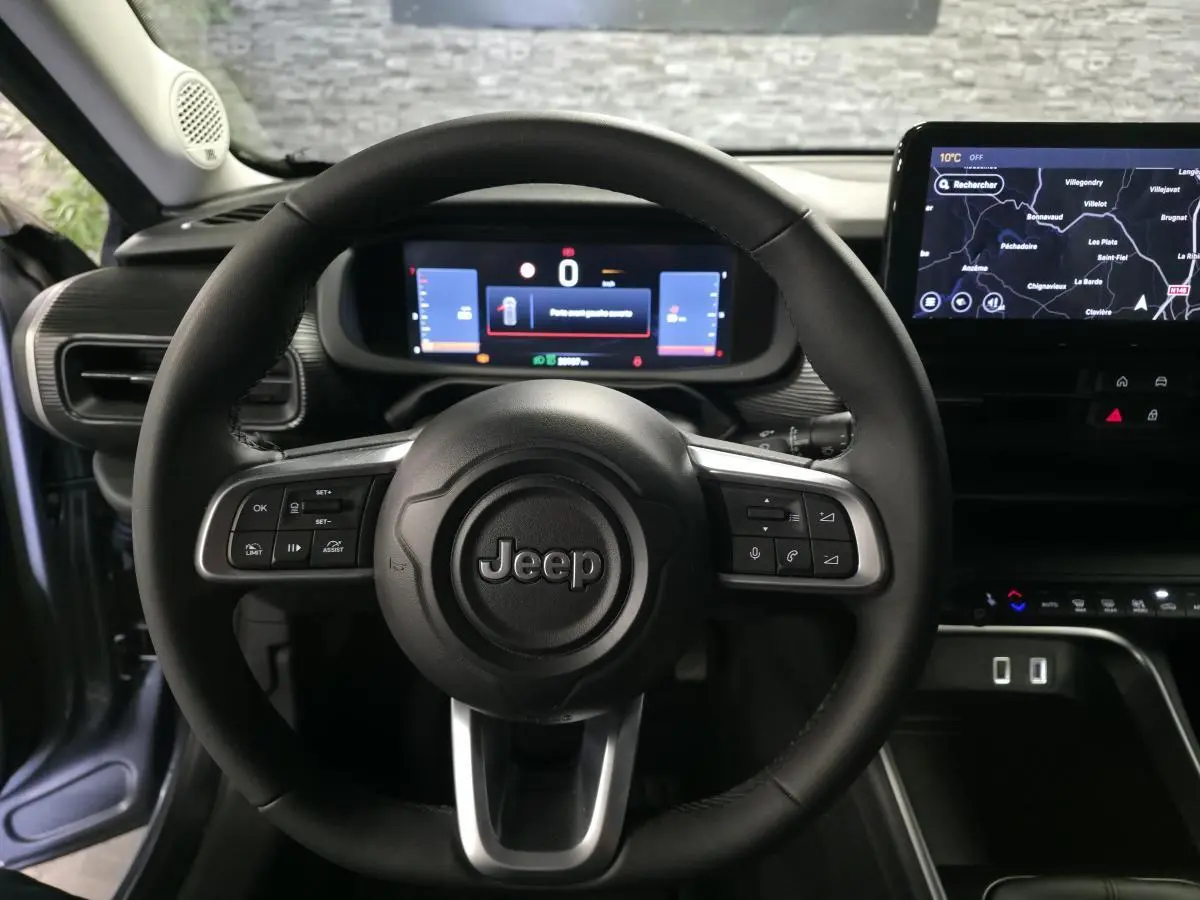 Vue intérieure centrée sur le volant Jeep noir avec tableau de bord numérique et écran tactile de navigation.