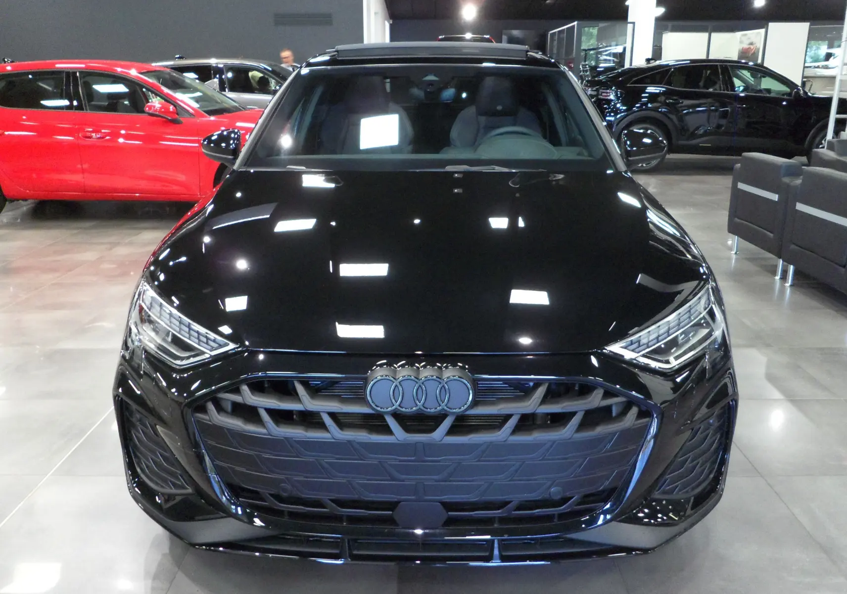 Vue frontale d'une Audi A3 Sportback 35 TFSI S-Line noire Mythe dans un showroom lumineux.
