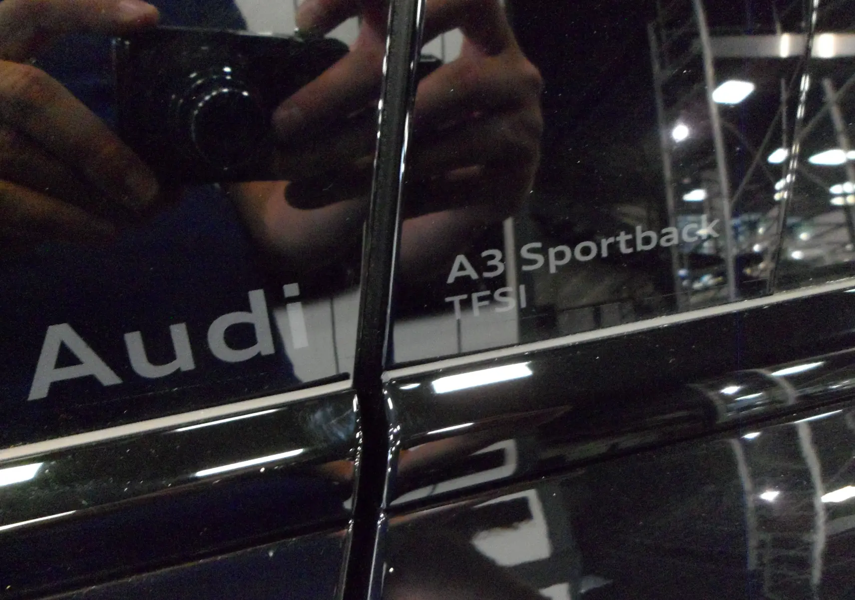Gros plan sur l'inscription A3 Sportback TFSI sur la porte noire Mythe d'une Audi 2025, reflet d'un photographe visible.