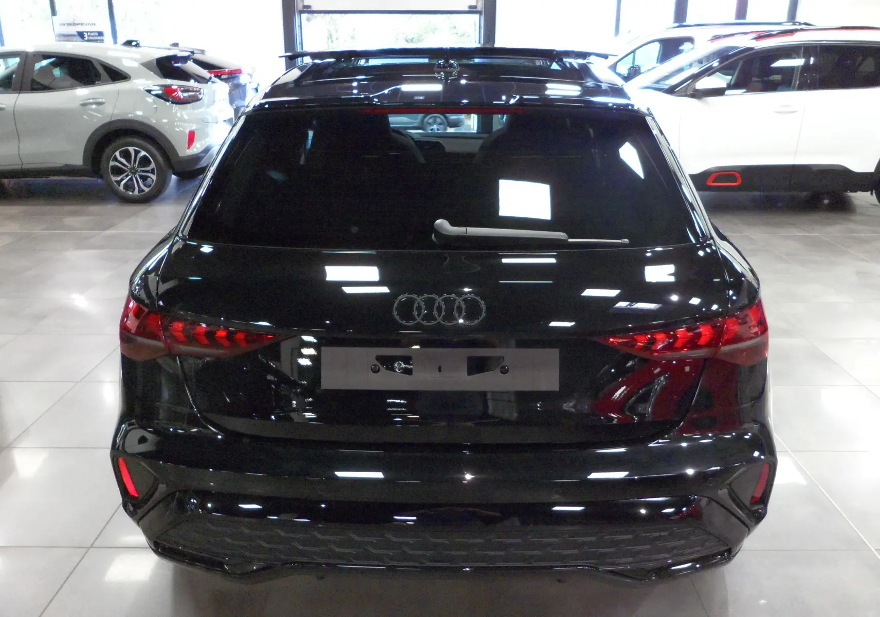 Vue arrière d'une Audi A3 Sportback 35 TFSI noir mythe, avec feux arrière LED et vitre teintée en showroom.