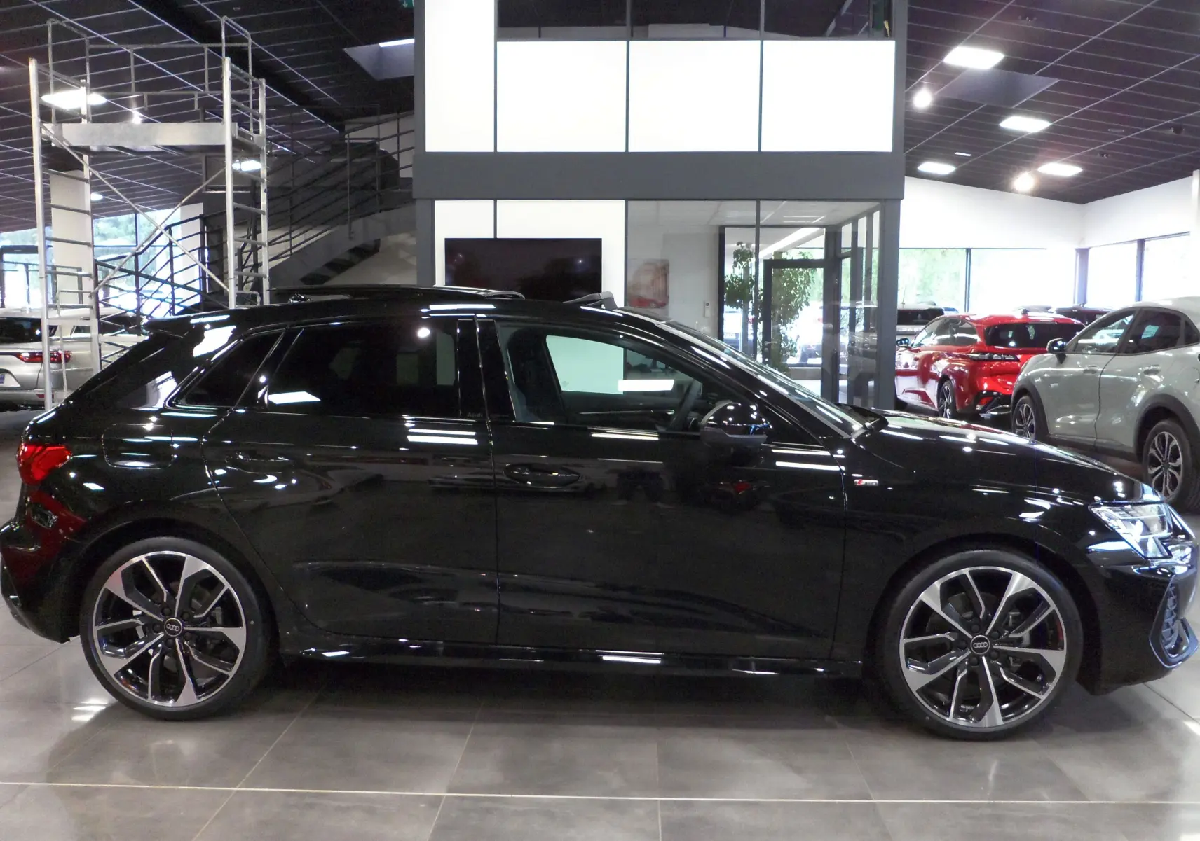 Audi A3 Sportback 35 TFSI noir mythe vue de profil côté gauche en intérieur avec jantes alliage bicolores.