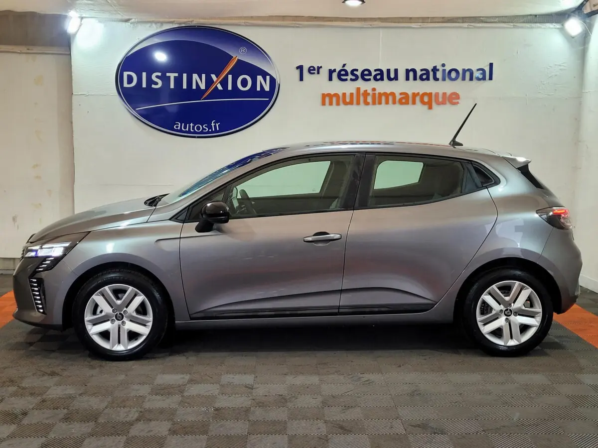 Profil droit d'une Renault Clio gris foncé 2025 garée en intérieur avec éclairage diffus et logo Distinxion en arrière-plan.