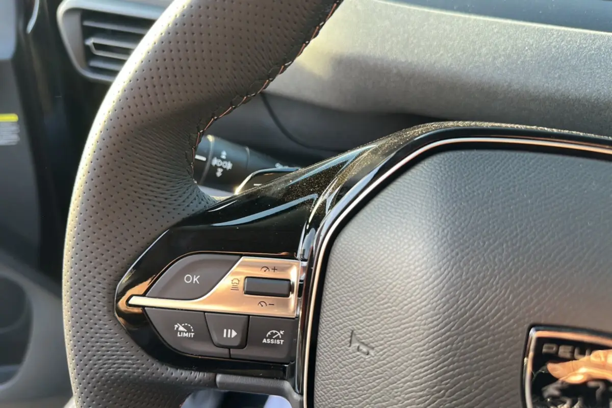 Gros plan sur le volant cuir perforé du Peugeot Rifter noir perla nera, avec commandes multifonctions visibles à gauche.