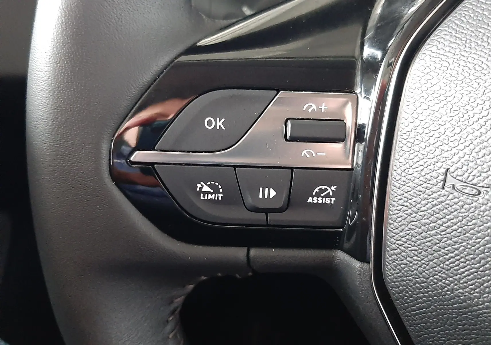 Gros plan sur les commandes au volant gauche d'une Peugeot 308 blanche, boutons de limitation et assistance visibles.