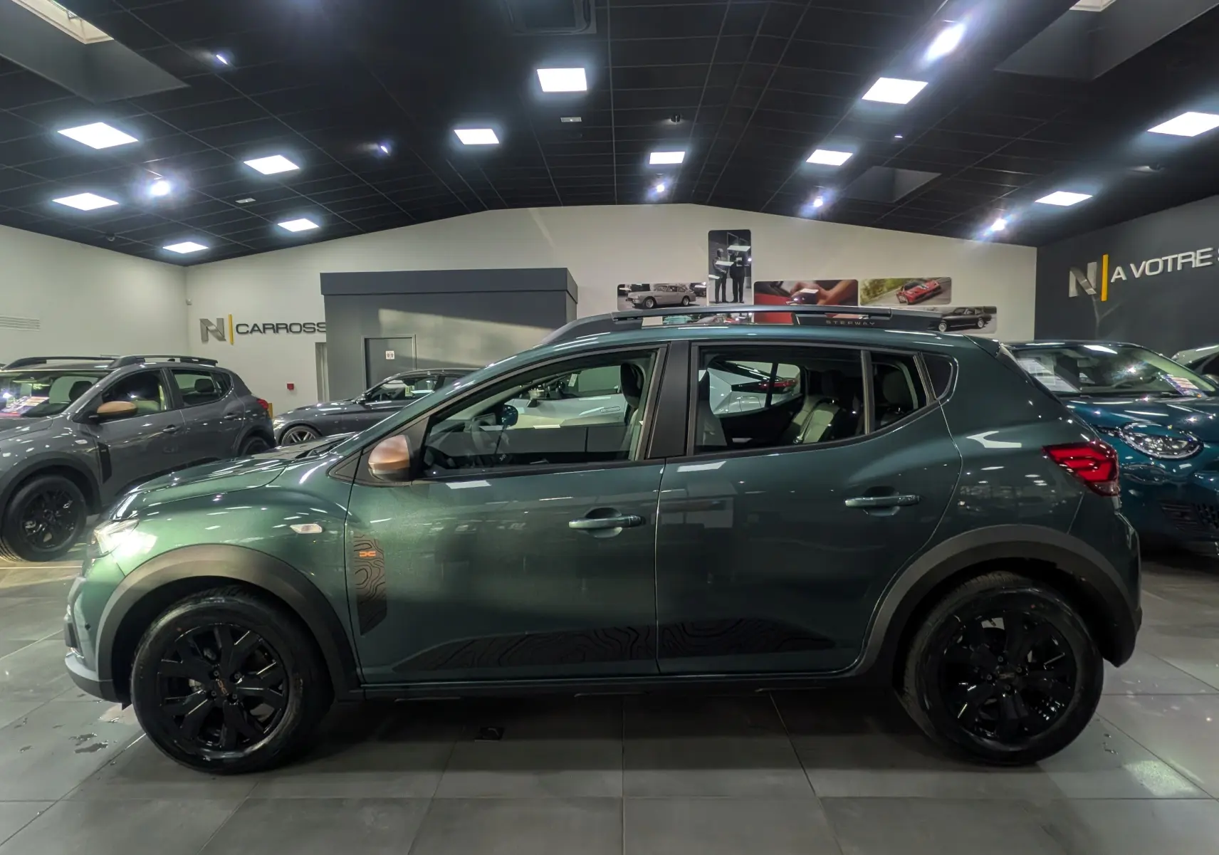 Profil côté gauche d'une Dacia Sandero Stepway TCe 110 Vert Cèdre avec jantes noires et coques de rétroviseurs bronze.