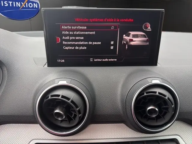 Écran tactile central affichant les aides à la conduite sur Audi Q2 blanc, vue intérieure du tableau de bord.