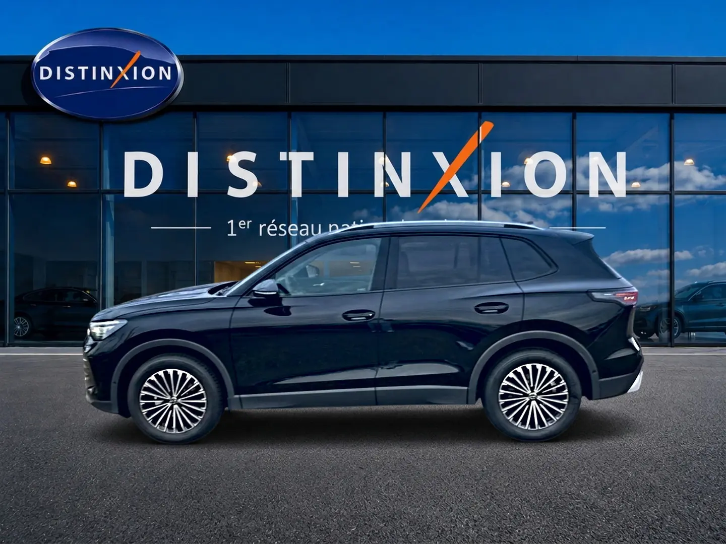 Vue de profil côté gauche d'un Volkswagen Tiguan noir 2025 garé devant une vitrine Distinxion.