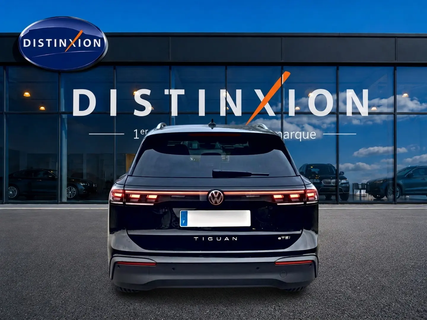 Vue arrière d'un Volkswagen Tiguan noir 2025 avec feux arrière LED et logo VW visible devant un bâtiment Distinxion.