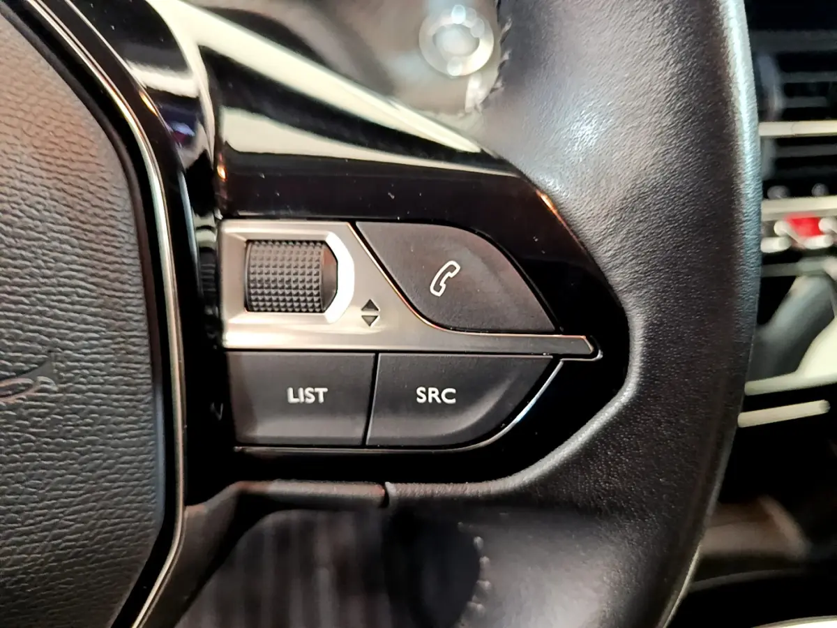 Gros plan sur les commandes gauche du volant cuir noir d'une Peugeot 208 blanche, boutons liste et appel visibles.
