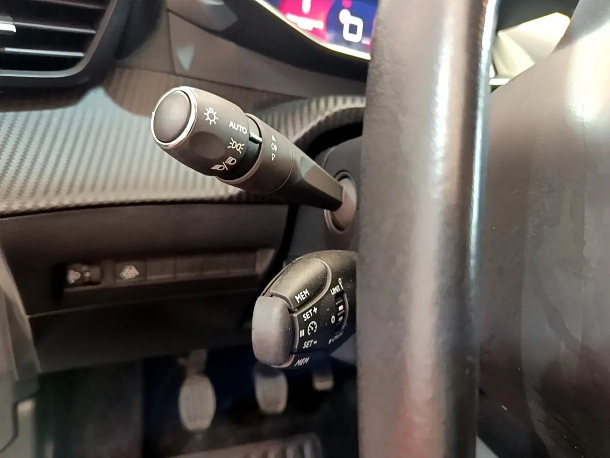 Gros plan sur les commandes au volant cuir de la Peugeot 208 blanc, avec leviers de clignotants et régulateur de vitesse.